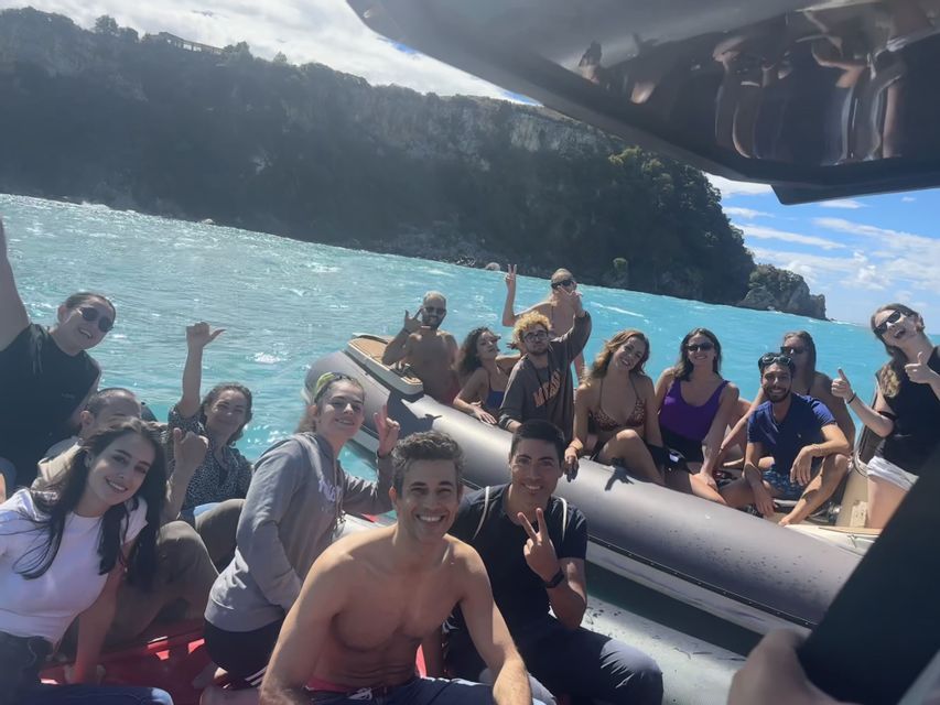 A WeRoad group trip posing for a photo on two inflatable boats on turquoise water near a tree-lined coast.