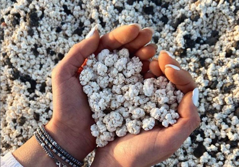 A person's cupped hands holding a handful of white, popcorn-like sand over a beach of similar white and black pebbles.