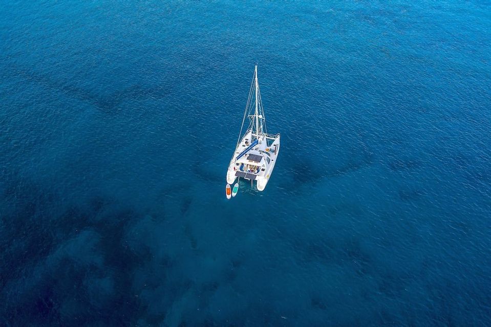 An aerial view of a white catamaran with a WeRoad group trip on board, anchored in a calm, clear blue sea.