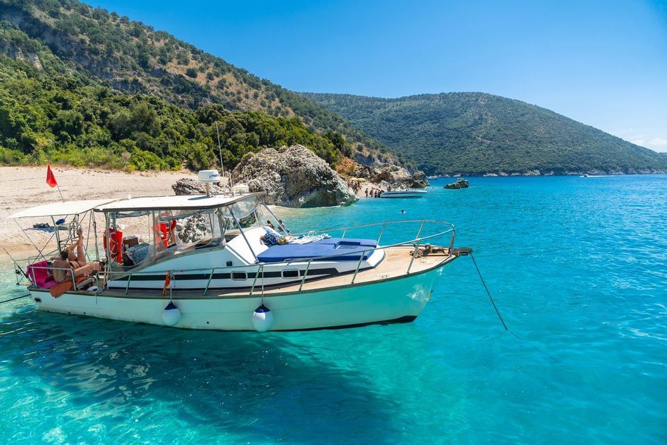 A boat carrying a WeRoad group trip is anchored in clear turquoise water near a hilly coastline with a small beach.