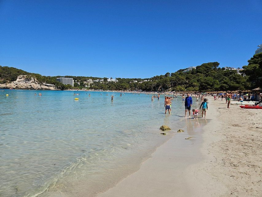 Molte persone nuotano e guadano nell'acqua cristallina turchese di una caletta affollata in una giornata di sole.