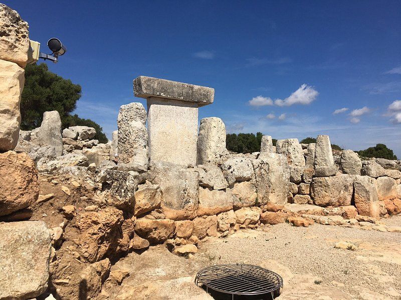 Un grande megalite a forma di T si erge tra antiche rovine di pietra in un sito archeologico sotto un cielo azzurro.