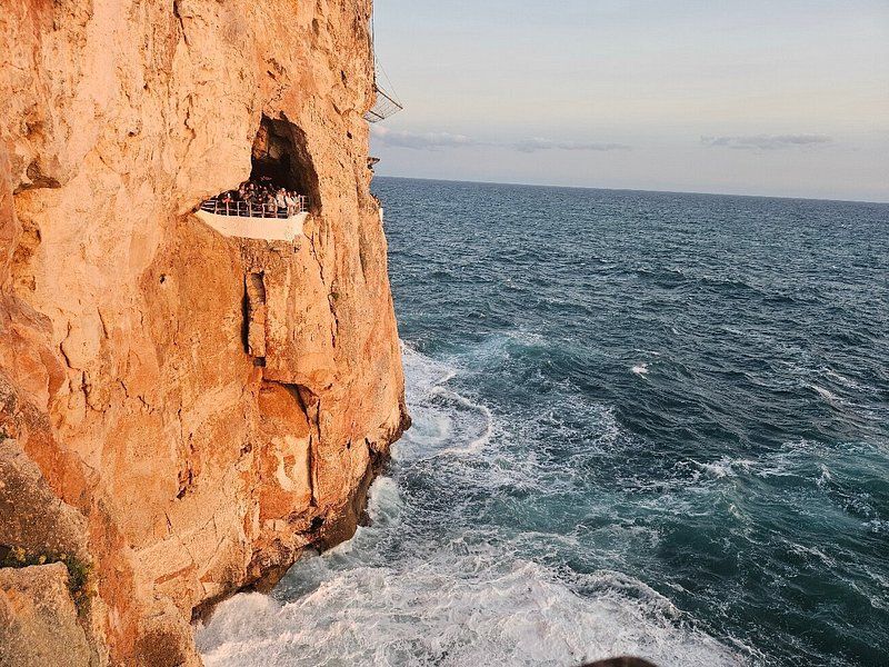Un viaggio di gruppo WeRoad su una piattaforma panoramica all'interno di una grotta su un'ampia scogliera a picco su un mare agitato.
