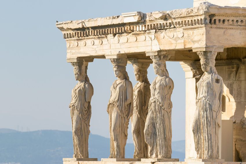 Cinque antiche cariatidi che sorreggono il tetto di un tempio classico sotto un cielo limpido e sereno