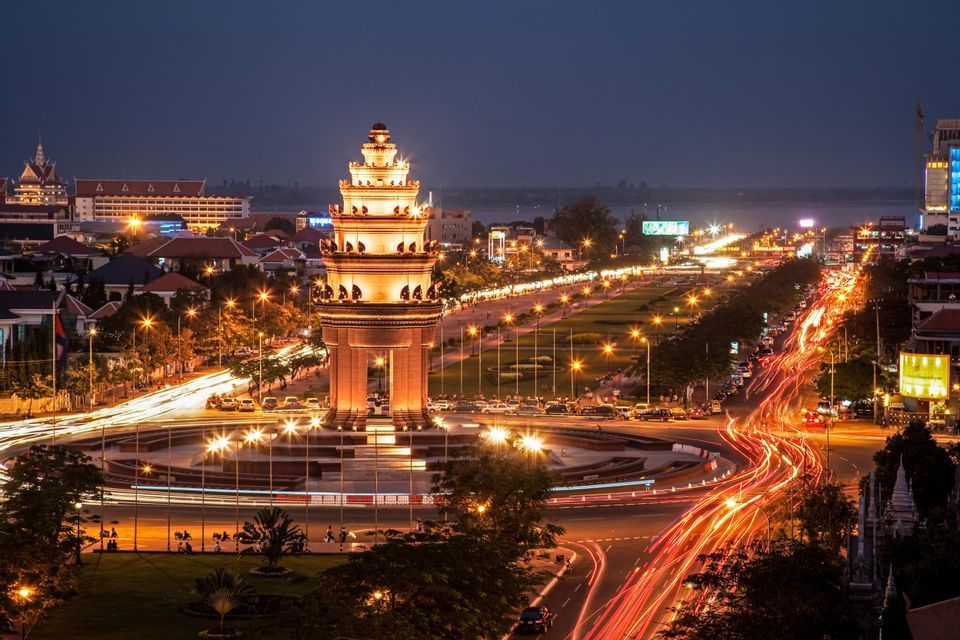 Un monumento iluminado en una rotonda de la ciudad por la noche, capturado con una exposición larga para mostrar estelas de luces de tráfico.