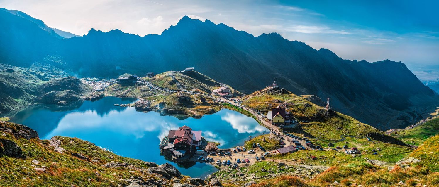 Una vista panorámica de un lago azul profundo rodeado de montañas verdes, con chalets y carreteras construidas a lo largo de su orilla.