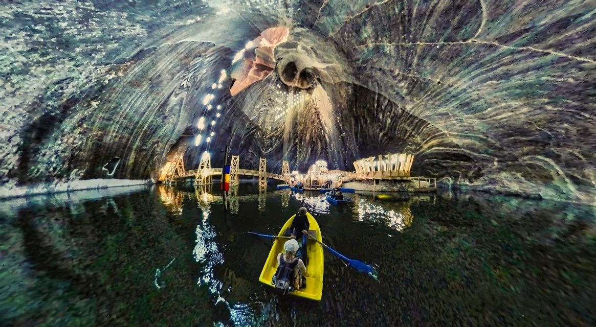 Vue grand angle de personnes en voyage de groupe WeRoad, pagayant sur un lac à l'intérieur d'une vaste caverne de sel souterraine illuminée.