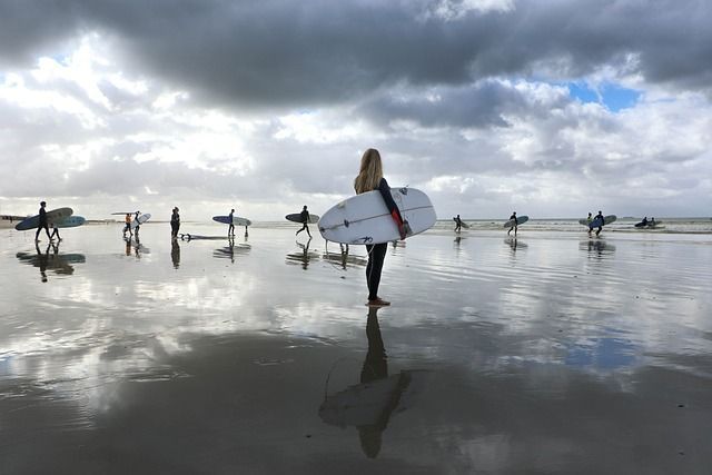Eine WeRoad Gruppenreise mit Surfern in Neoprenanzügen, die ihre Boards an einem nassen Strand tragen und sich im Sand spiegeln.