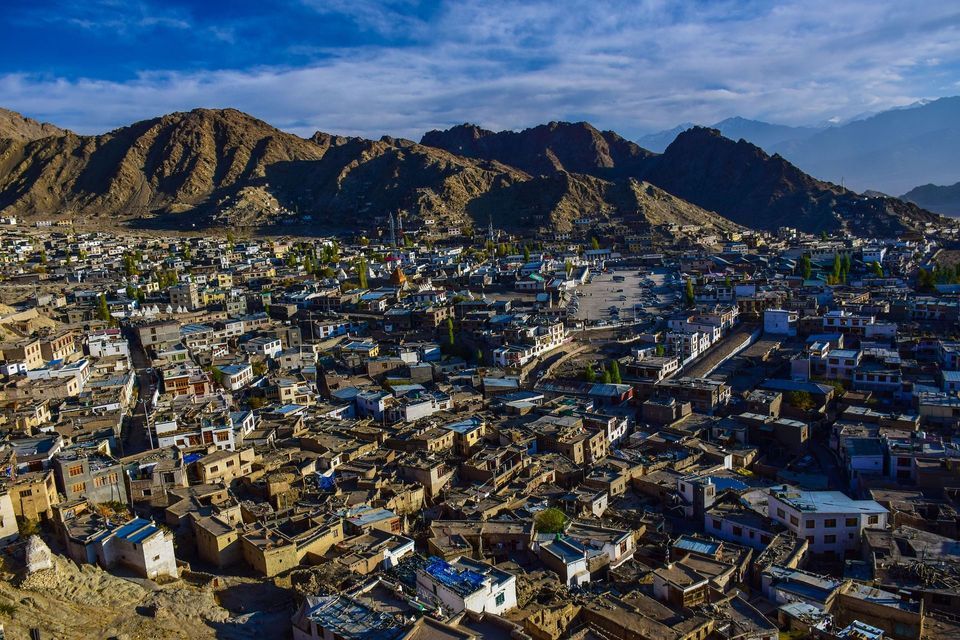 Una vista aerea di una citta densa con edifici bassi situata in una valle ai piedi di grandi montagne rocciose