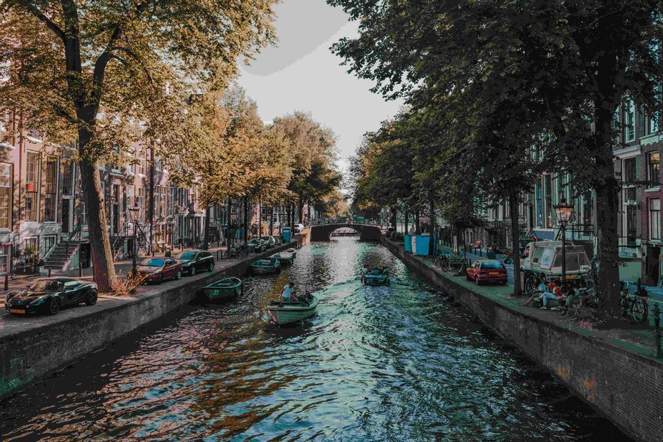 Un canal arbolado en una ciudad, con barcos en el agua y coches aparcados junto a edificios tradicionales.