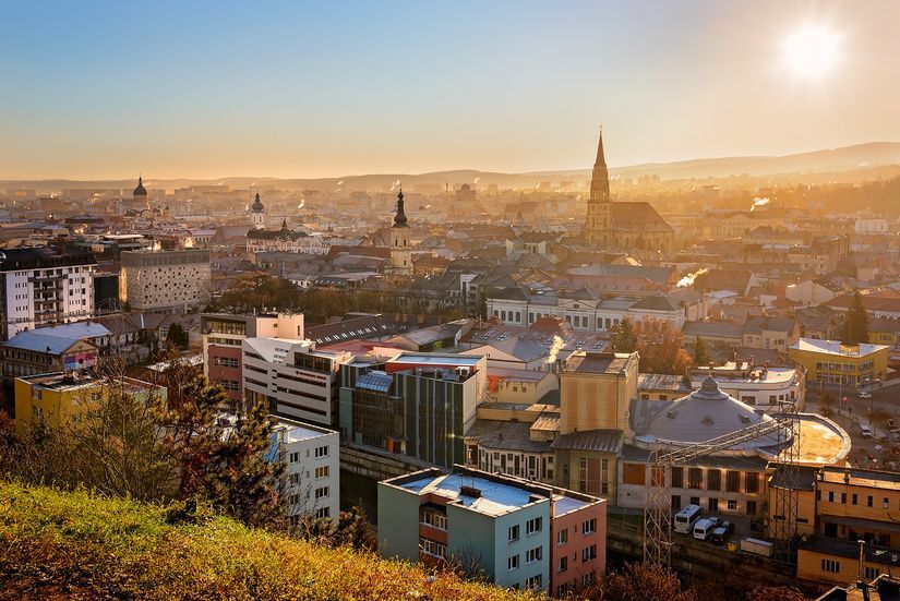 Vista panoramica di una città con un campanile prominente, bagnata dalla luce dorata del sole basso.