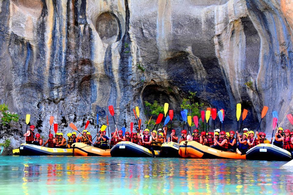 Un viaggio di gruppo WeRoad su gommoni tiene in alto pagaie colorate di fronte a un'alta scogliera rocciosa.