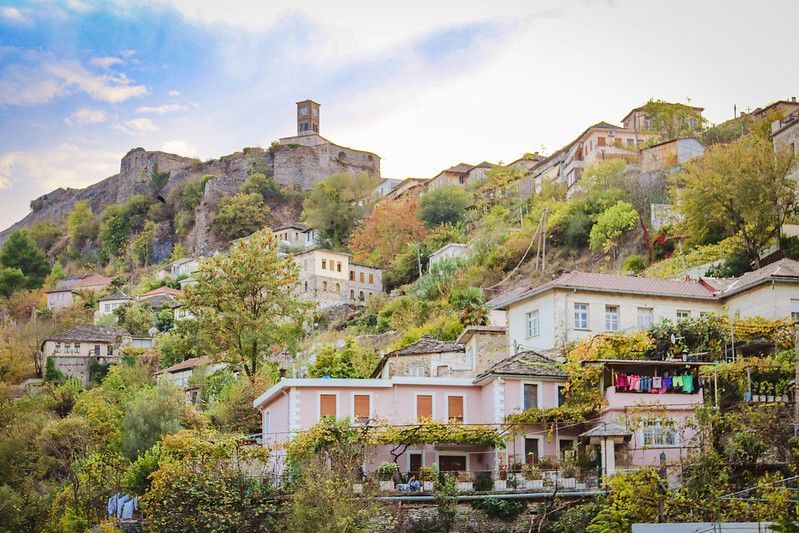 Un borgo storico con case tradizionali costruito su una rigogliosa collina verde sotto un castello in pietra con una torre dell'orologio.