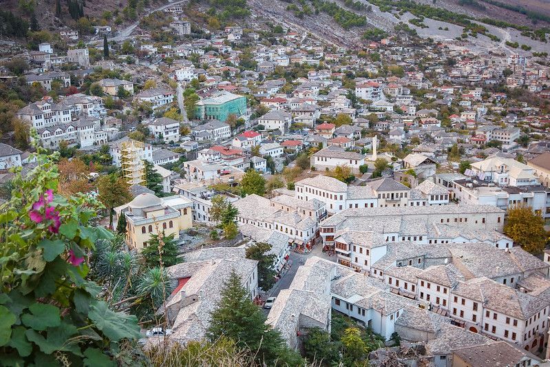 Vue aérienne d'une ville historique aux bâtiments blancs et aux toits de pierre, nichée dans une colline verdoyante et luxuriante.