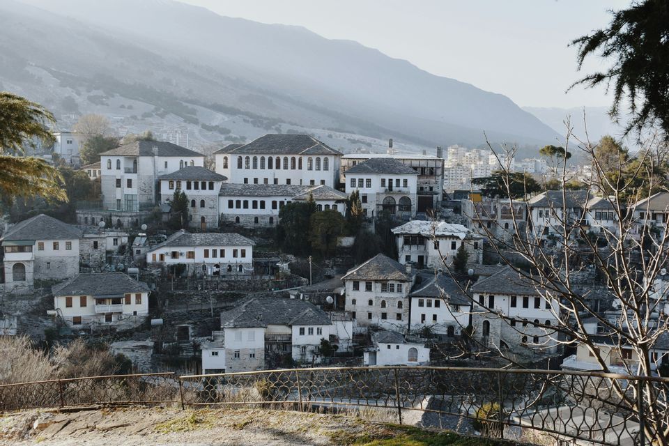Un villaggio collinare di case in pietra bianca con tetti scuri, con una grande montagna nebbiosa sullo sfondo.