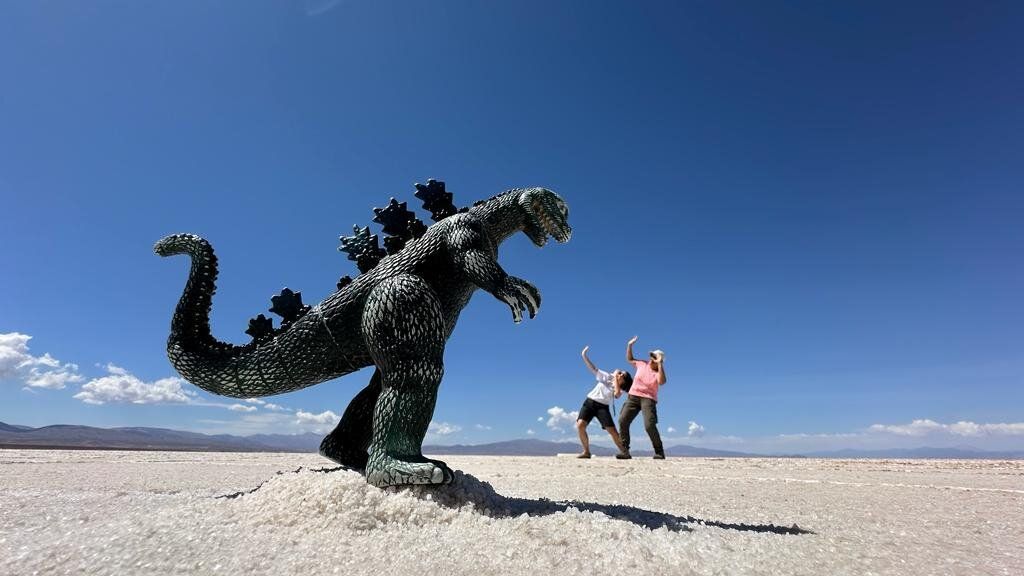 Un viaje en grupo de WeRoad utiliza perspectiva forzada con un juguete de Godzilla en un salar, con dos personas fingiendo estar asustadas.