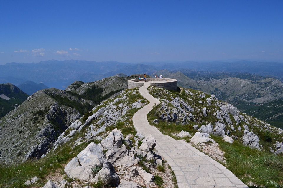 Ein gewundener Steinweg auf einem felsigen Berg führt zu einem runden Aussichtspunkt, wo sich eine WeRoad-Reisegruppe versammelt hat.