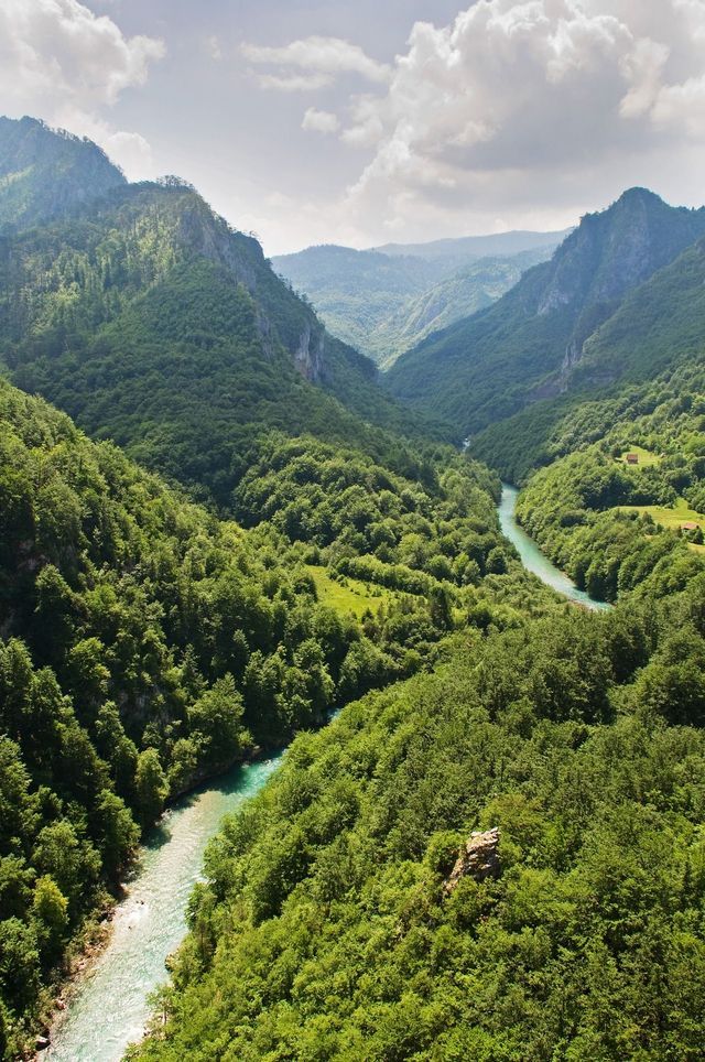 Ein türkiser Fluss schlängelt sich durch eine tiefe, üppig bewaldete Schlucht unter einem teils bewölkten Himmel.
