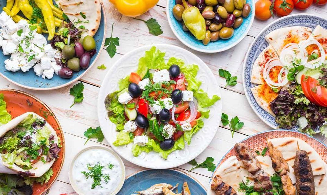 Una vista dall'alto di un tavolo imbandito con piatti greci, tra cui insalata greca, souvlaki, pane pita e olive.