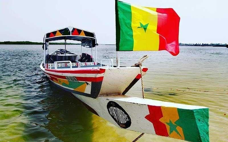 Ein farbenfrohes Boot mit der senegalesischen Flagge am Bug schwimmt in ruhigem Wasser.