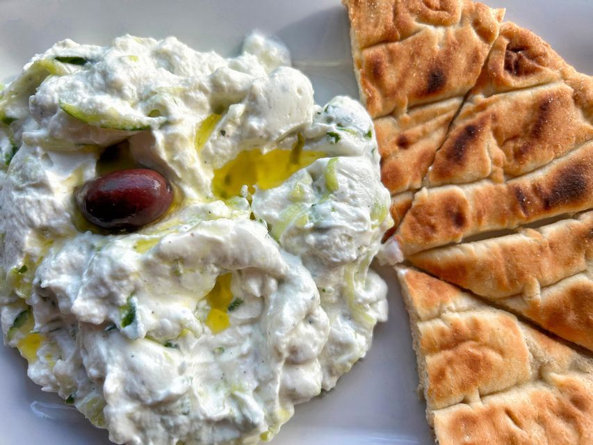 Salsa tzatziki cremosa, irrorata con olio d'oliva e guarnita con un'oliva, servita con pane pita grigliato.