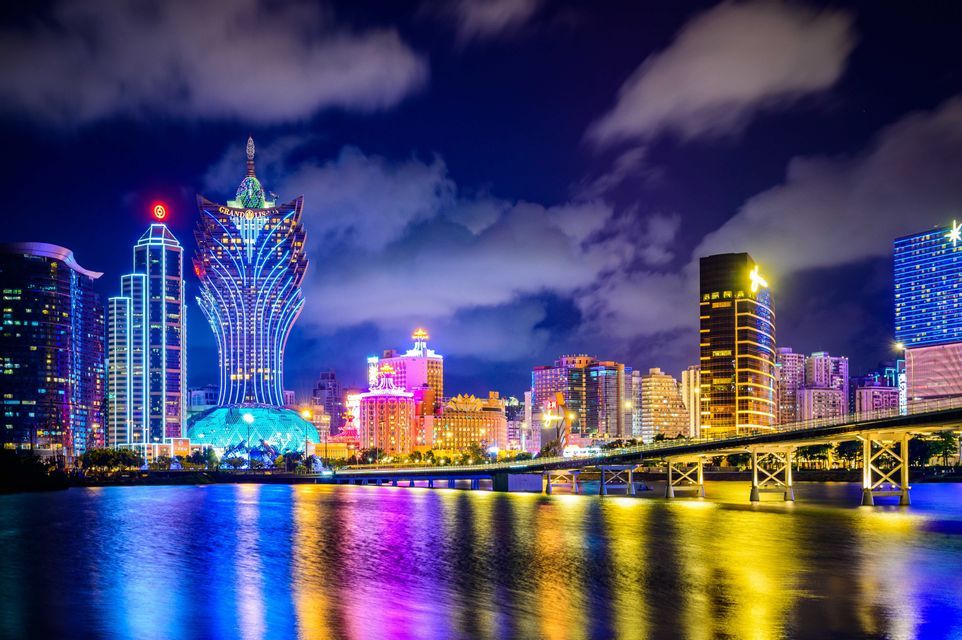 Panorama urbain nocturne avec néons colorés se reflétant sur l'eau, et un pont.