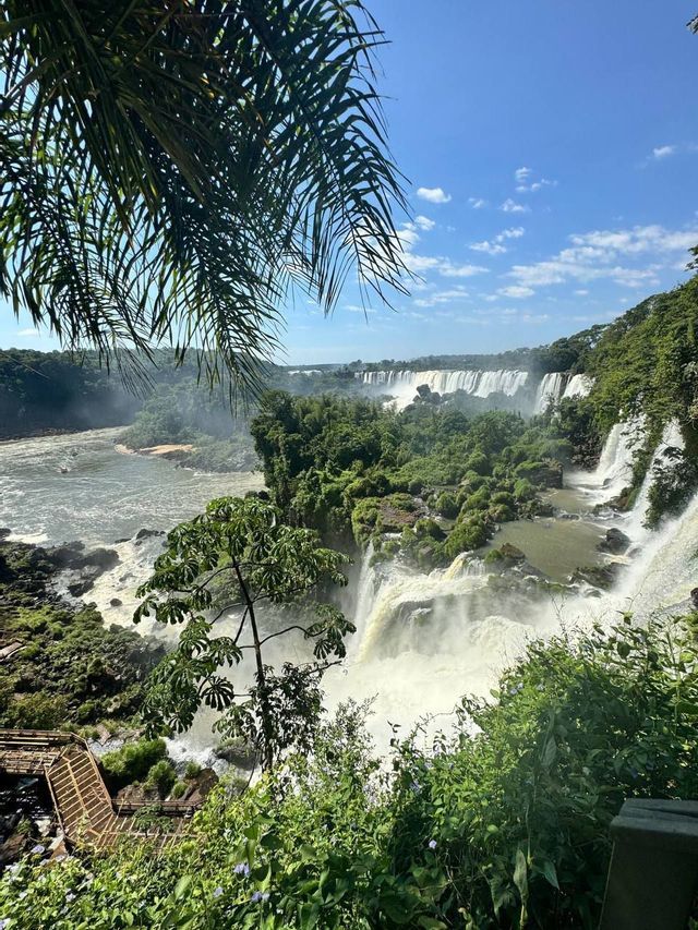 Una vista panorámica de un gran sistema de cascadas en una selva exuberante, con agua cayendo a un río bajo un cielo azul.