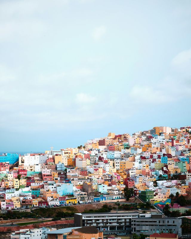 A dense cluster of colorful buildings covers a hillside beneath a pale blue sky with light clouds.