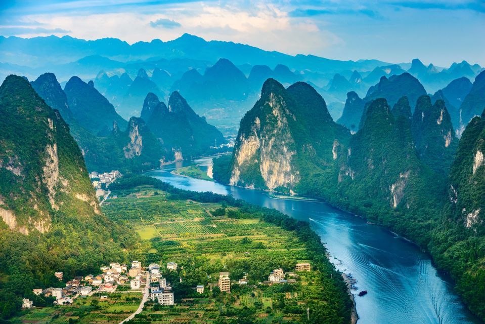 Une vue aérienne d'une rivière sinuant à travers une vallée de montagnes karstiques verdoyantes, avec de petits villages et des champs sur les rives.