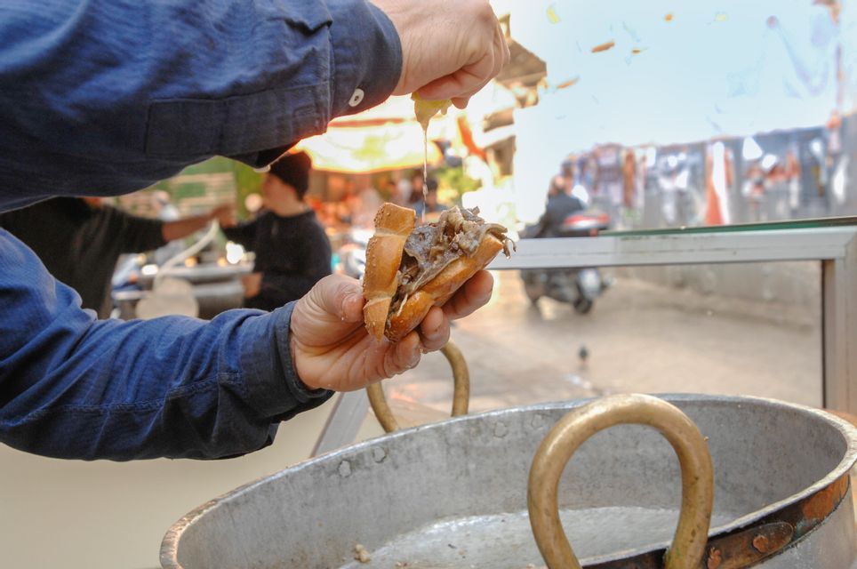 Un venditore spreme un limone su un panino ripieno di carne in una bancarella di street food all'aperto.