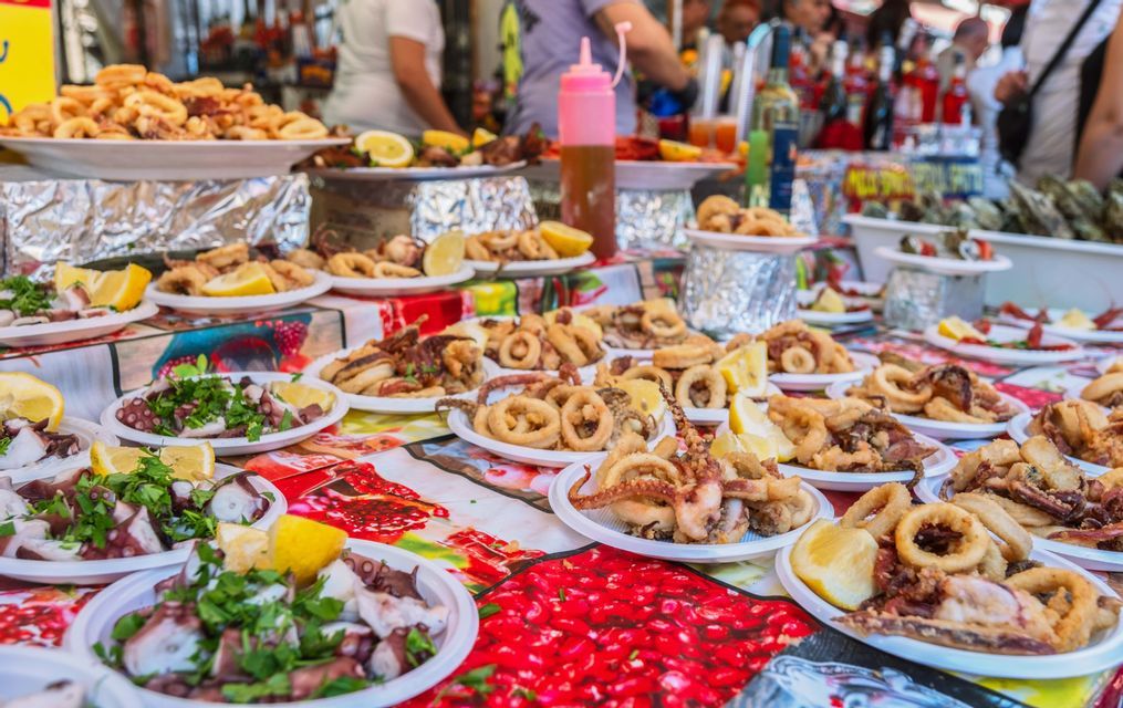 Una varietà di piatti di pesce fritto, inclusi calamari e insalata di polpo al limone, esposti in un mercato di street food.