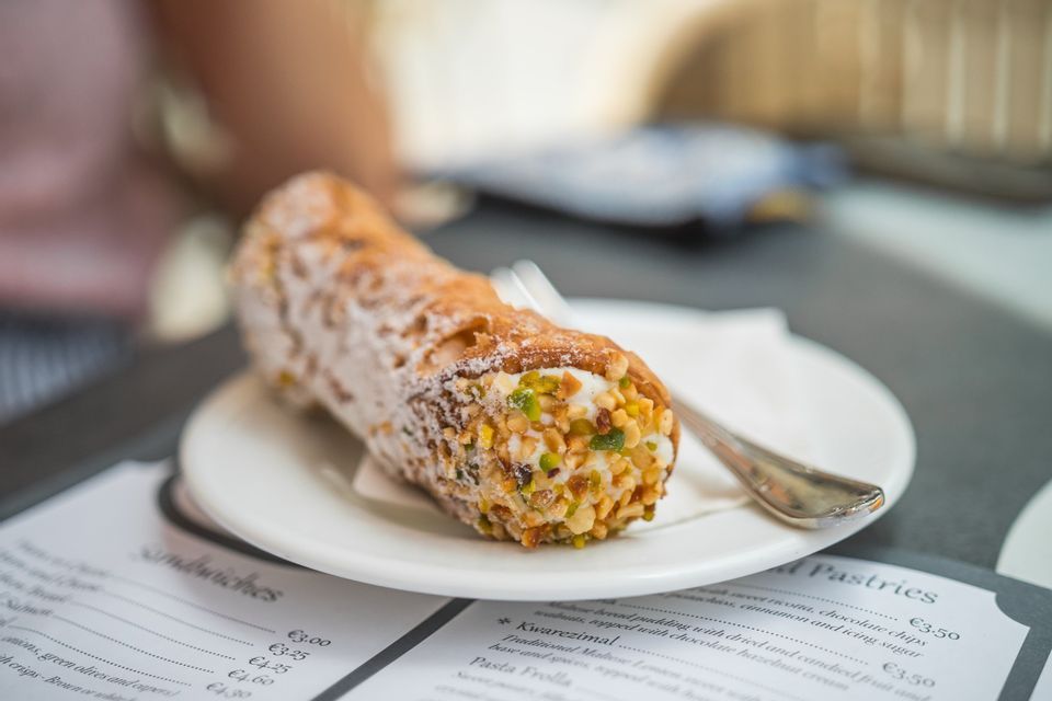 Primo piano di un cannolo con pistacchi su un piatto bianco con una forchetta, appoggiato su un menu.