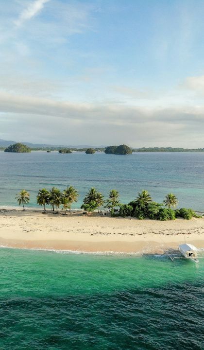 Veduta aerea di una lingua di sabbia tropicale con palme, una spiaggia di sabbia bianca e una barca ormeggiata in acqua turchese.