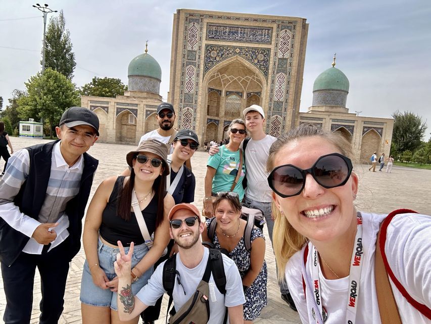 Un grupo de WeRoad posa para una selfie sonriente en una plaza frente a un edificio histórico con cúpulas turquesas.
