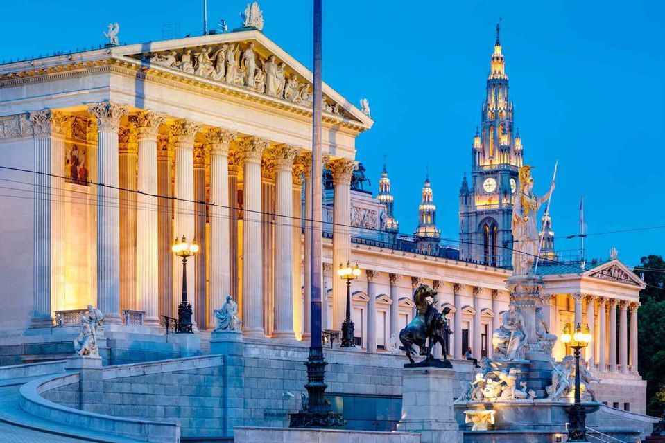 A grand neoclassical building with columns and a tall clock tower illuminated against a deep blue dusk sky.