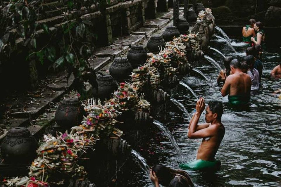 Un viaggio di gruppo WeRoad partecipa a un rituale di purificazione dell'acqua, facendo il bagno sotto una serie di getti di pietra decorati in una sorgente sacra.