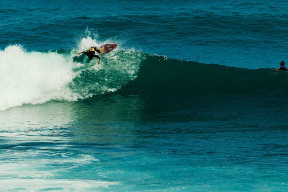 Un surfista in muta cavalca abilmente la cresta di una grande onda spumeggiante nell'oceano blu.