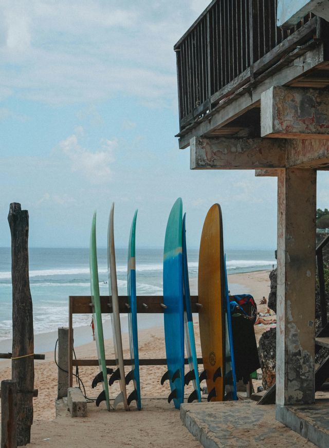 Tavole da surf colorate in un portatavole di legno su una spiaggia sabbiosa con vista sull'oceano.
