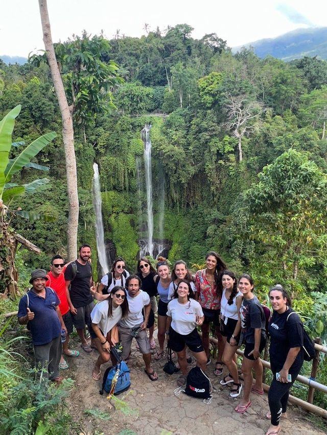Un grupo de WeRoad posando para una foto en un sendero frente a una gran cascada en una exuberante selva verde.