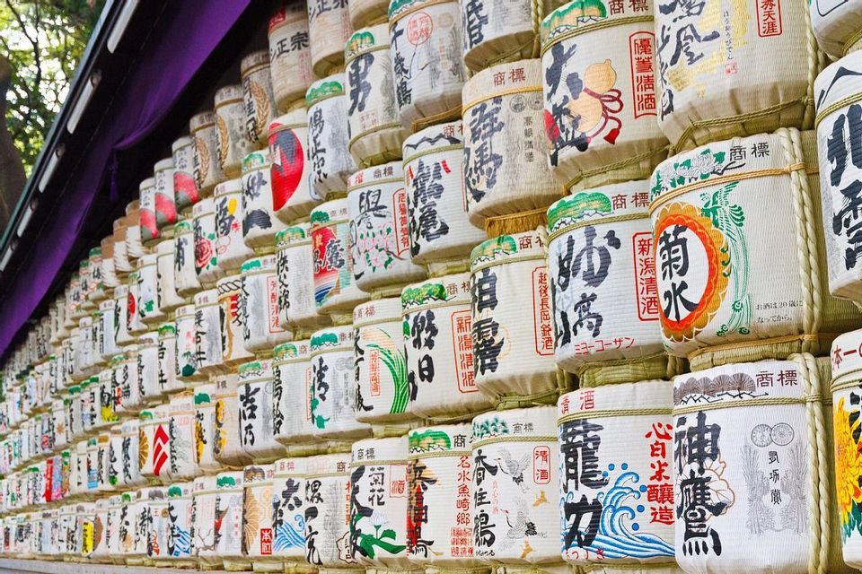 Una parete di botti decorative di sake giapponese impilate in file, ognuna con calligrafia colorata e disegni tradizionali