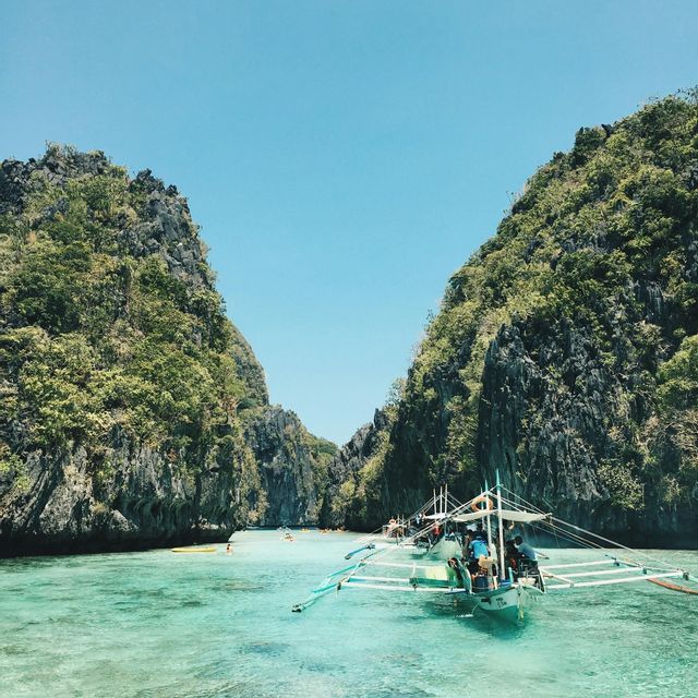 Un viaggio di gruppo WeRoad su diverse canoe a bilanciere galleggia su una laguna turchese tra alte scogliere rocciose e verdi.