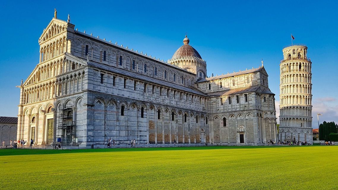 La Cattedrale di Pisa e la Torre Pendente di Pisa si ergono su un ampio prato verde sotto un cielo azzurro limpido.