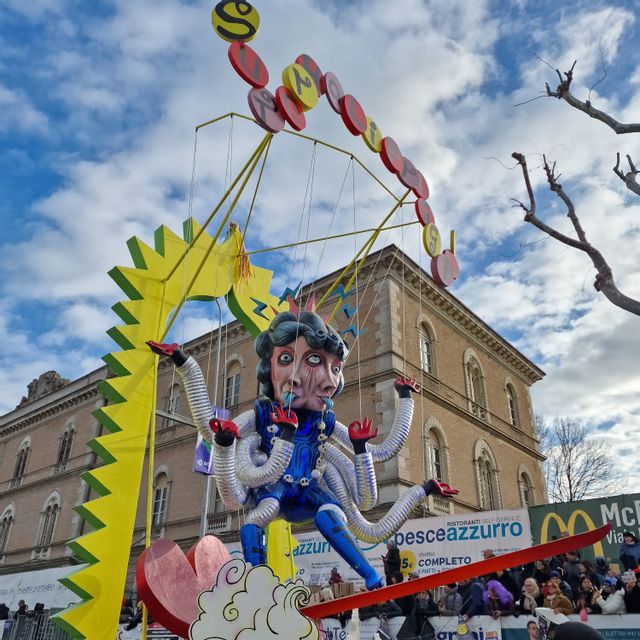 Un grande carro di carnevale surreale raffigurante una figura con molte facce e braccia, come una marionetta, in una sfilata di strada.