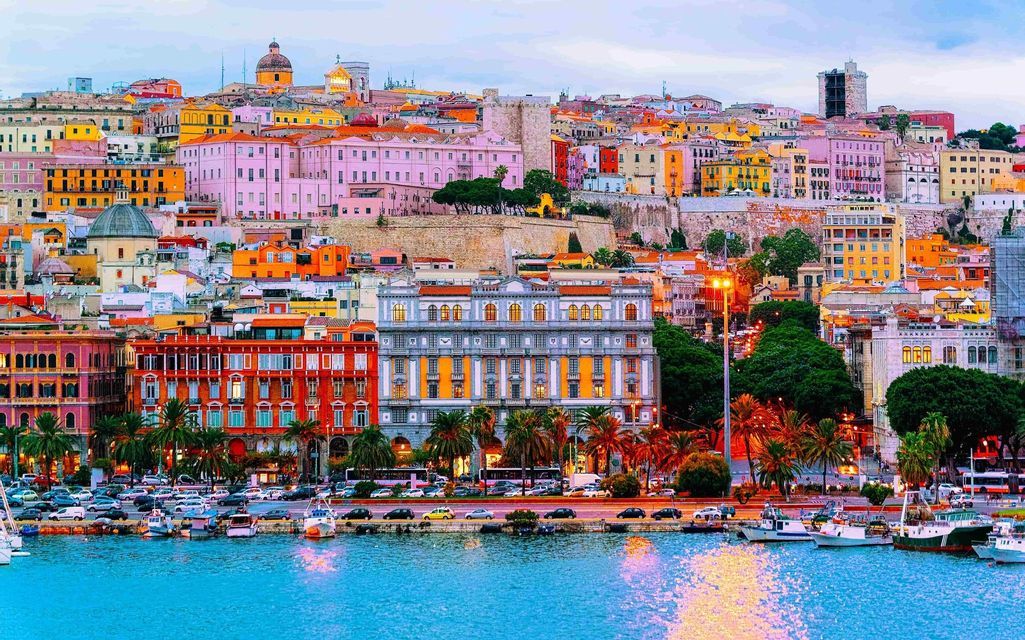 A colorful city built on a hillside overlooking a harbor with many boats docked along the waterfront.