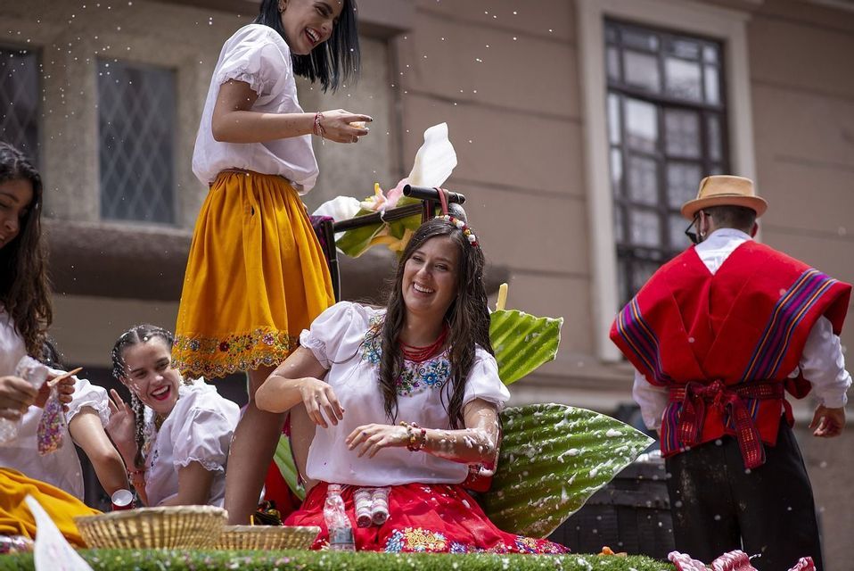 Diverse donne sorridenti in abiti tradizionali festeggiano su un carro allegorico, coperte di schiuma festosa.