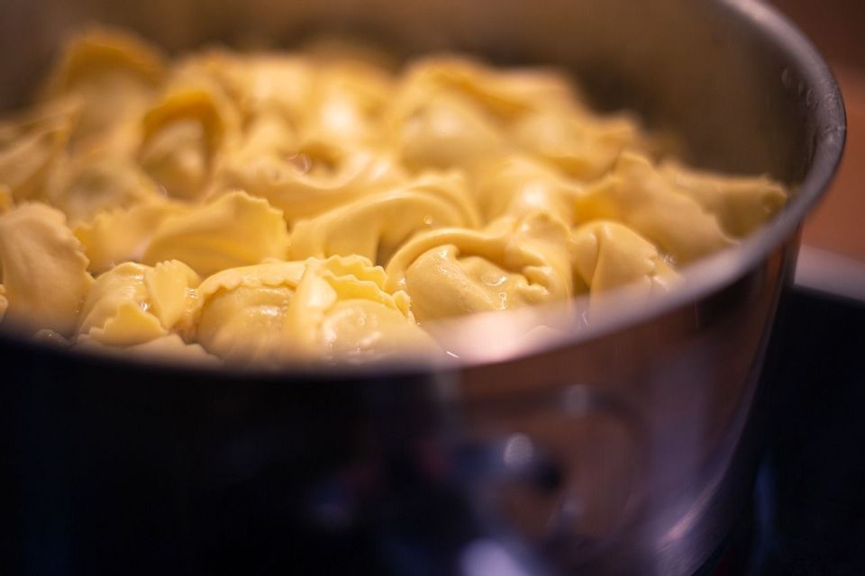 Un primo piano di tortellini freschi che bollono in una pentola d'acqua in acciaio inossidabile.