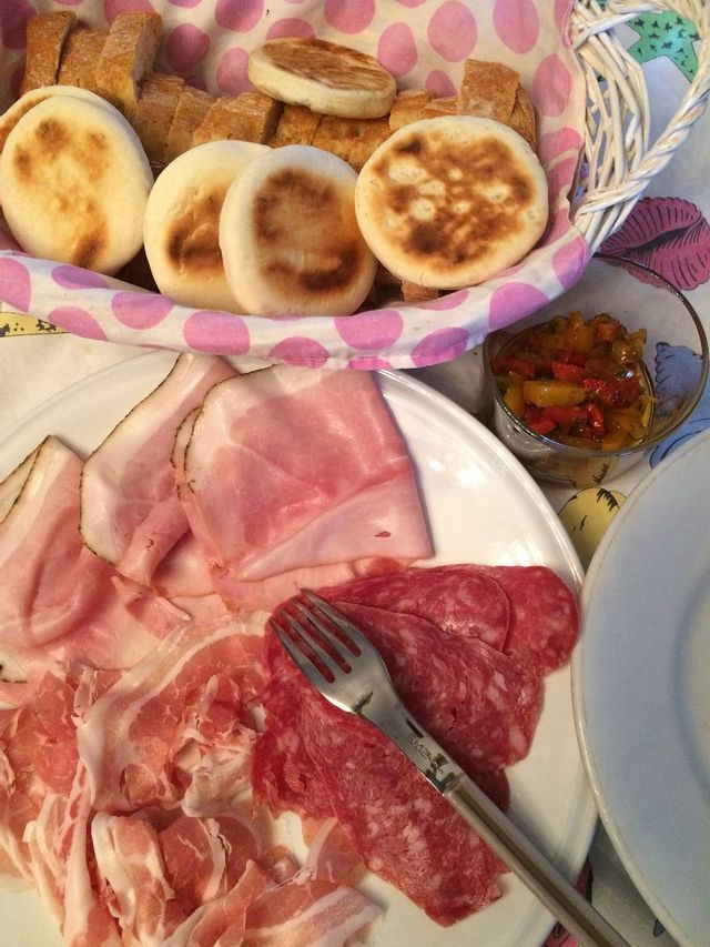 Un tagliere di prosciutto e salame affettati è accompagnato da un cestino di tigelle e un contorno di giardiniera.