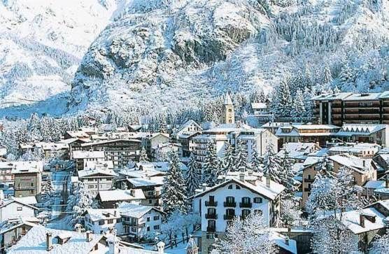 Un villaggio innevato con chalet e pini si trova ai piedi di una grande montagna.