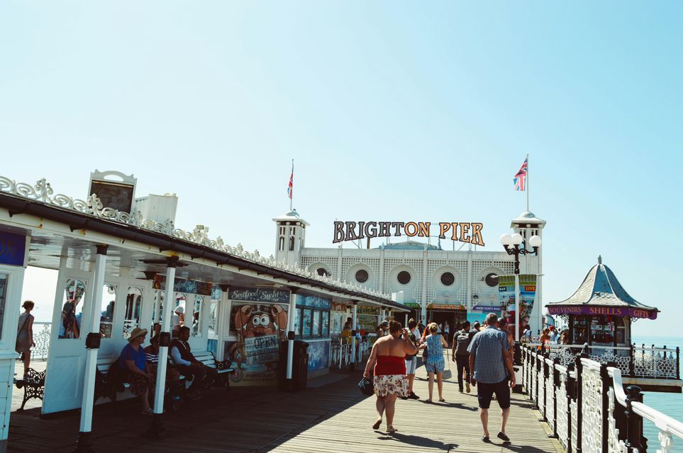 La gente passeggia lungo il lungomare soleggiato verso l'ingresso principale del Molo di Brighton.