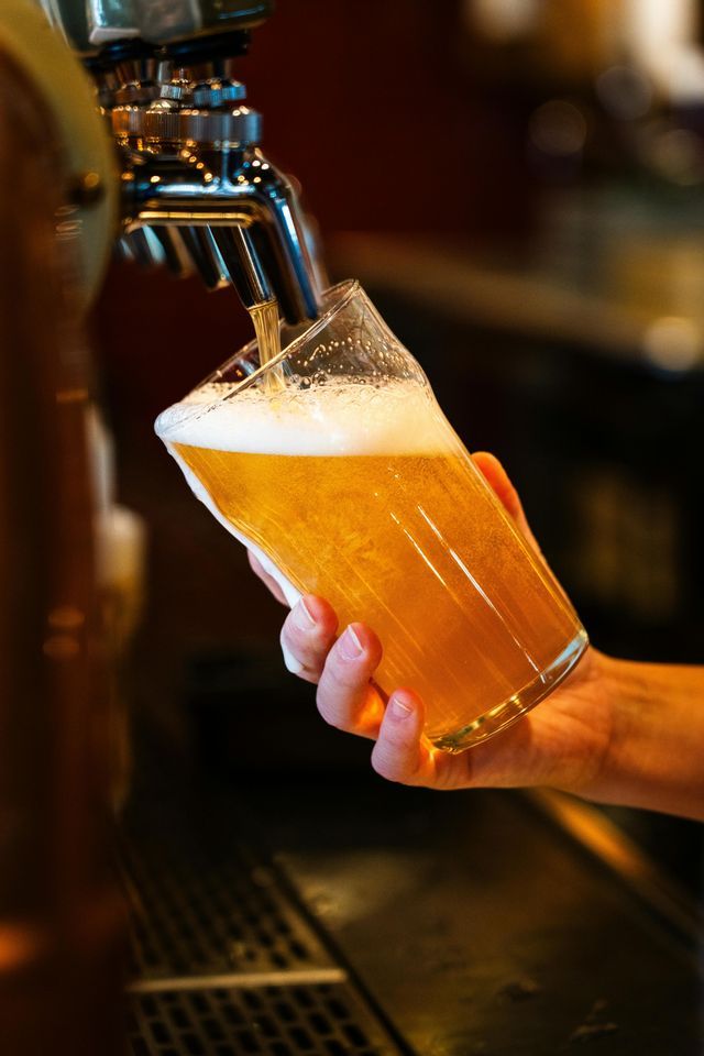 Primo piano di una mano che regge un boccale da pinta mentre viene riempito di birra dorata e schiumosa da un rubinetto cromato.